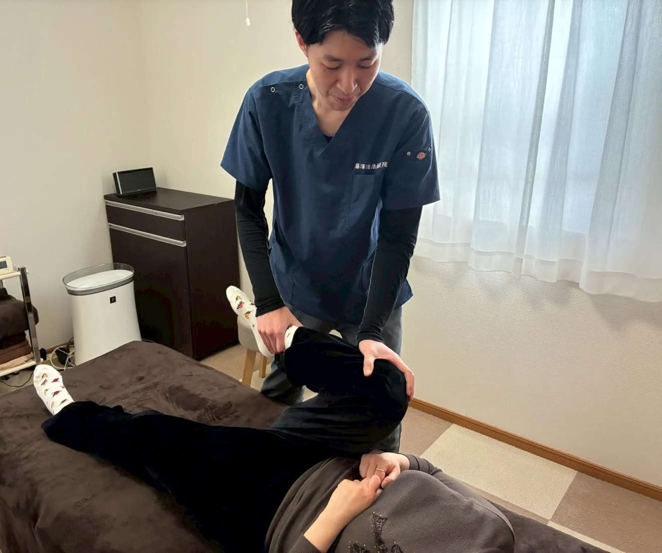 院長が、施術ベッドに仰向けになった方の脚に手を添えて施術している様子